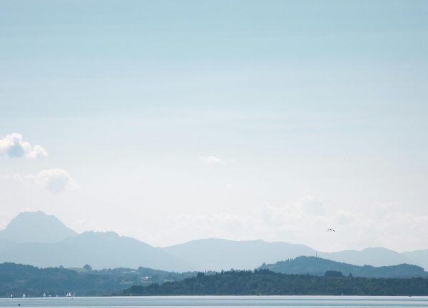 Calm waters of Chiemsee Lake with the Bavarian Alps in the background under a clear sky.